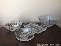 Top and angled view of four crystal pieces including three bowls and one rectangular tray on wood surface.
