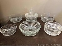 Front view of six crystal bowls including one with lid on wood surface. Variety of cut glass patterns visible.
