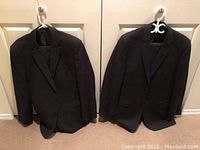 Two men's suit jackets hanging on door hooks, black and navy blue colors