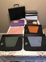 Overview photo showing black briefcase, photo albums, three-ring binders, and paper folders arranged on a table.