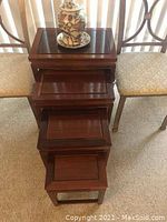 Stacked set of four rosewood nesting tables with ceramic vase on top and two metal chairs flanking