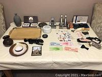 Photo showing assortment of pottery, metal presses, wooden tray, office tools, grooming items, currency, and lottery tickets on table.