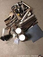 Photo showing assorted welding tools and metal rods, brushes, clamps, rods, face shield and other metal parts on garage floor.