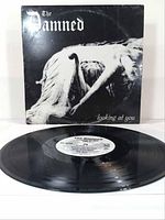Photo of The Damned "Looking At You" vinyl record partially pulled out from the album sleeve, sleeve in good condition with black monochrome art.