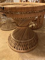 Hourglass-shaped wicker pedestal table with radial top pattern, shown alongside other pieces.