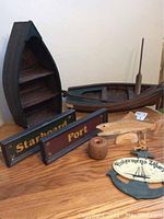 Wooden boat-shaped shelf with multiple shelves, painted wood Port and Starboard signs, cork buoy with rope, painted wooden fish, Fishermen's Wharf sign, and decorative wooden boat with oars on a table.