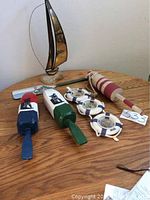 Wide view of all nautical items on a wooden table including the brass sailboat, the painted wooden buoys, the life ring clock, and the painted oar.