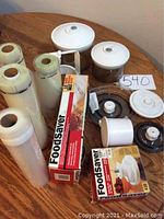 Photo showing FoodSaver brand vacuum sealing accessories, two white containers with lids, and cylindrical canisters on a wooden table.
