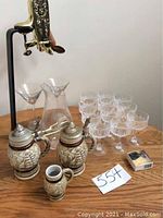 Full lot showing beer steins, stein cup, wine decanter, crystal champagne glasses, martini glasses, and whiskey stones
