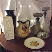 Photo of the full lot showing seven decorative items including vases, candleholders, and a plate all on a round table.