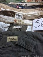Close up of brand labels inside waistbands of shorts showing Chaps, Dockers, Urban, Wrangler labels, and different colors including beige and olive green.