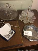 Mikasa candle holders in original box; two-tiered serving plate with clear glass ruffled edges; covered glass pedestal cake holder with dome cover; Kromekraft silver-tone tray with decorative pierced border
