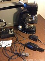 Bausch & Lomb black microscope with power cords and lamp placed on brown table