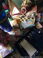 View of various games including checkerboard, backgammon, card decks, Jenga blocks, plastic pails, chalkboard, and paperwork.