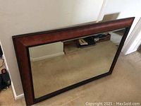 Front view of the dark wood framed mirror sitting on carpeted floor against a wall.