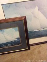 Two matted and framed sailing prints. Larger print features a sailboat with full sails in the water. Smaller print with dark wood frame and navy mat shows a cutter yacht.