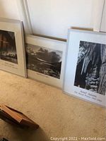 Three framed Ansel Adams prints leaning on a carpeted floor showing iconic black and white landscape photography