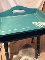 Photos of a turquoise wooden child's desk with a white elephant design on the tray surface and visible wear and scratches.
