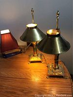 Two gold-colored Orient Express lamps on wooden table, with conical metal shades and ornate square bases with claw feet.