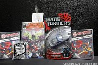Wide shot showing all collected Transformers items including an action figure, comic book, DVDs, and Happy Meal toy against a dark black backdrop.