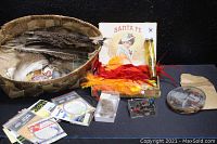 Full view of the basket filled with assorted fishing flies, Santa Fe boxes, bottle, and other fishing paraphernalia arranged for display.