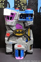 Front view of the Fisher-Price Imaginext DC Superfriends Batcave playset, showing the gray cave-shaped structure with colored play features and Batman logo.