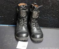 Front view of the pair of black leather Harley-Davidson boots showing lace-up design and metal emblem buckle on shin area.