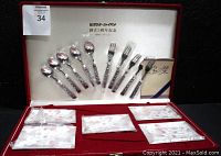 Photo of the open red velvet box showing five floral cloisonne plates and ten cloisonne-handled silverware pieces (5 forks, 5 spoons) plus paperwork inside.