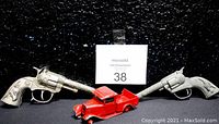 Photo of two metal cap guns and one red die-cast metal 1932 Ford truck toy, placed on a black background with lot number card.
