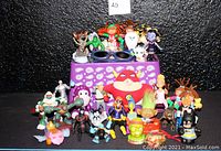 Photo of a purple paisley bin filled with 35 assorted pre-owned toys including Happy Meal toys, PVC figurines, novelty sunglasses, and collectible figures from popular franchises.