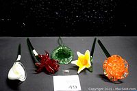Five crystal clear glass flower stems displayed in a row on a black surface, showing variety of colors and designs.