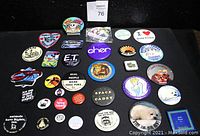 Full view of the assortment of vintage pin backs, political and humorous message pins, themed magnets, and one patch.