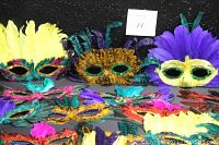 Photo showing front view of multiple masquerade masks in bright colors, feathers, and sequins.
