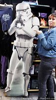 Full view of the life-size Stormtrooper cardboard cutout shown with packing tape covering, held by a woman to show scale and condition.