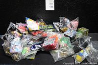 Pile of over 30 assorted kid's meal toys in varying conditions and packaging, mostly in individual plastic bags, on a black background.