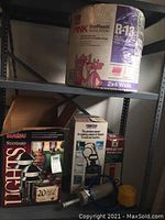 Photo of shelving showing the Owens Corning pink R-13 insulation roll on top shelf with boxes of lighting and manual pump below.