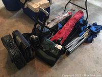 Wide view of lot showing folded chairs, umbrellas, thermos tote, and screenhouse tent with poles.