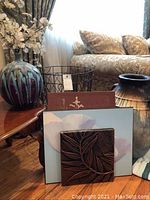 Two decorative vases, wire basket, and three wall art pieces on a table near a couch