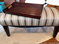 View of dark wooden serving tray resting on striped upholstered bench