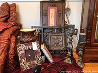 Photo of various metal wall art pieces, framed décor, large wooden candlesticks with green candles, and a planter or umbrella stand.
