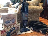 Full view showing all four items: Sunbeam humidifier box, Dirt Devil handheld vacuum box, Bissell floor cleaner upright, and Oreck XL vacuum with attachments.