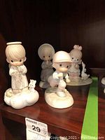 Four Precious Moments figurines displayed on a wooden shelf, showing all figurines together.