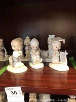 Full view of 5 Jonathan and David figurines displayed on a wood shelf, including children with a dog, seated child reading, and a child in graduation cap holding a scroll.