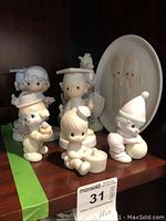 Eight Precious Moments figurines displayed on a wooden surface along with one plate standing behind them