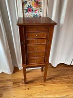 Front view of wood jewelry cabinet showing six drawers with metal knobs and side doors.