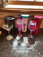 Three Lolita Collection martini glasses with colorful hand-painted designs on countertop beside their tall cylindrical boxes