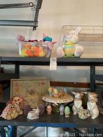 Easter decor arranged on two shelves including ceramic bunnies and chicks, cake platter with eggs, and container of Beanie Babies.