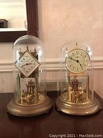 Photo showing two anniversary clocks under glass domes, sitting next to each other.