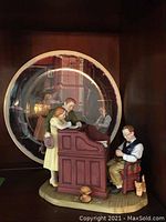 Figurine and decorative plate set displayed together, showing detailed Victorian/early 20th century style scene with three figures and small dog.