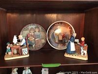 Shelf display with two Norman Rockwell figurines and two plates behind them